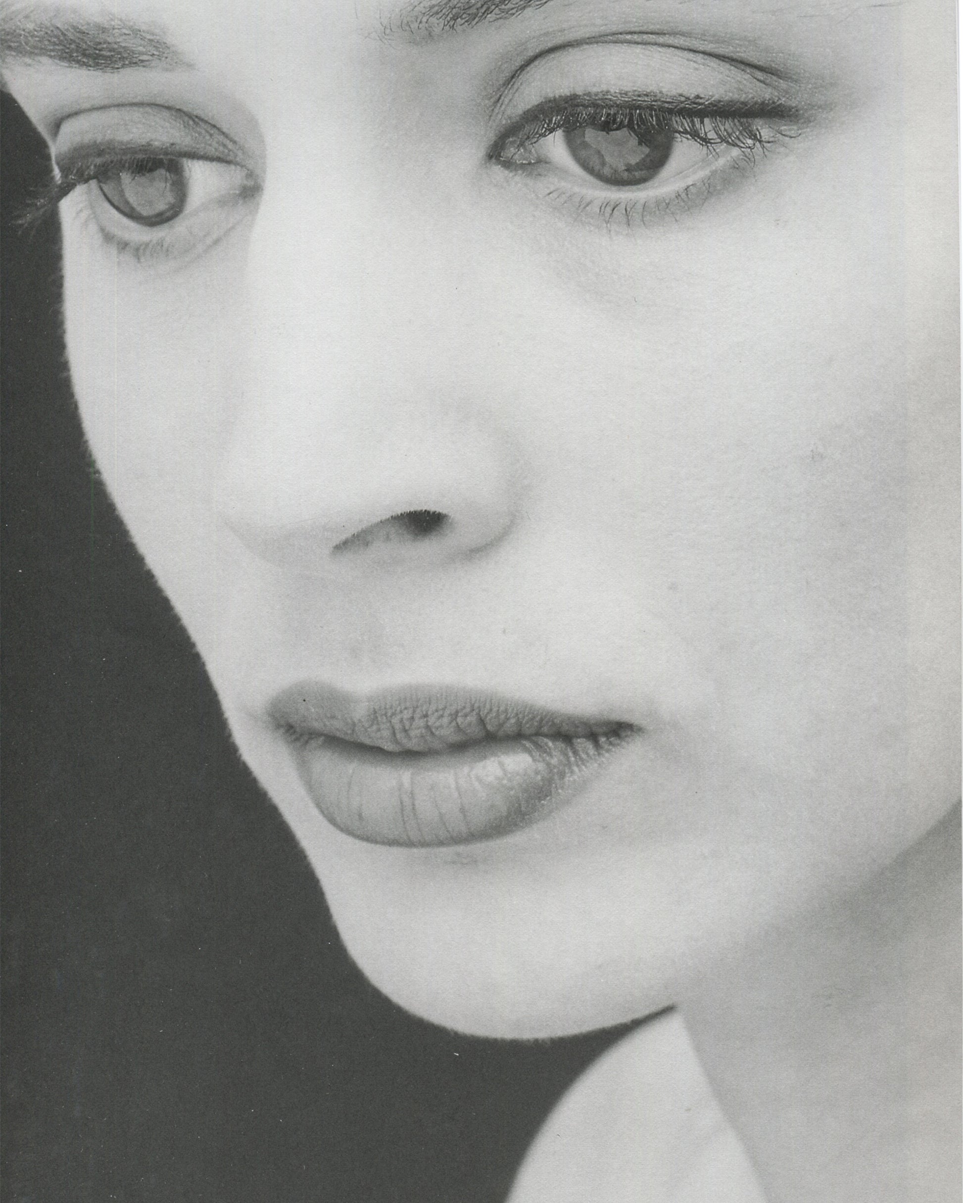 Interior page from Robert Mapplethorpe, Some Women, Bulfinch Press, 1992, showing a black-and-white extreme close-up of a woman's face cropped from the brow to the chin, the eyes gazing directly at the camera with a calm, neutral expression, the face lit to emphasise skin texture and the geometry of the features against a dark background.