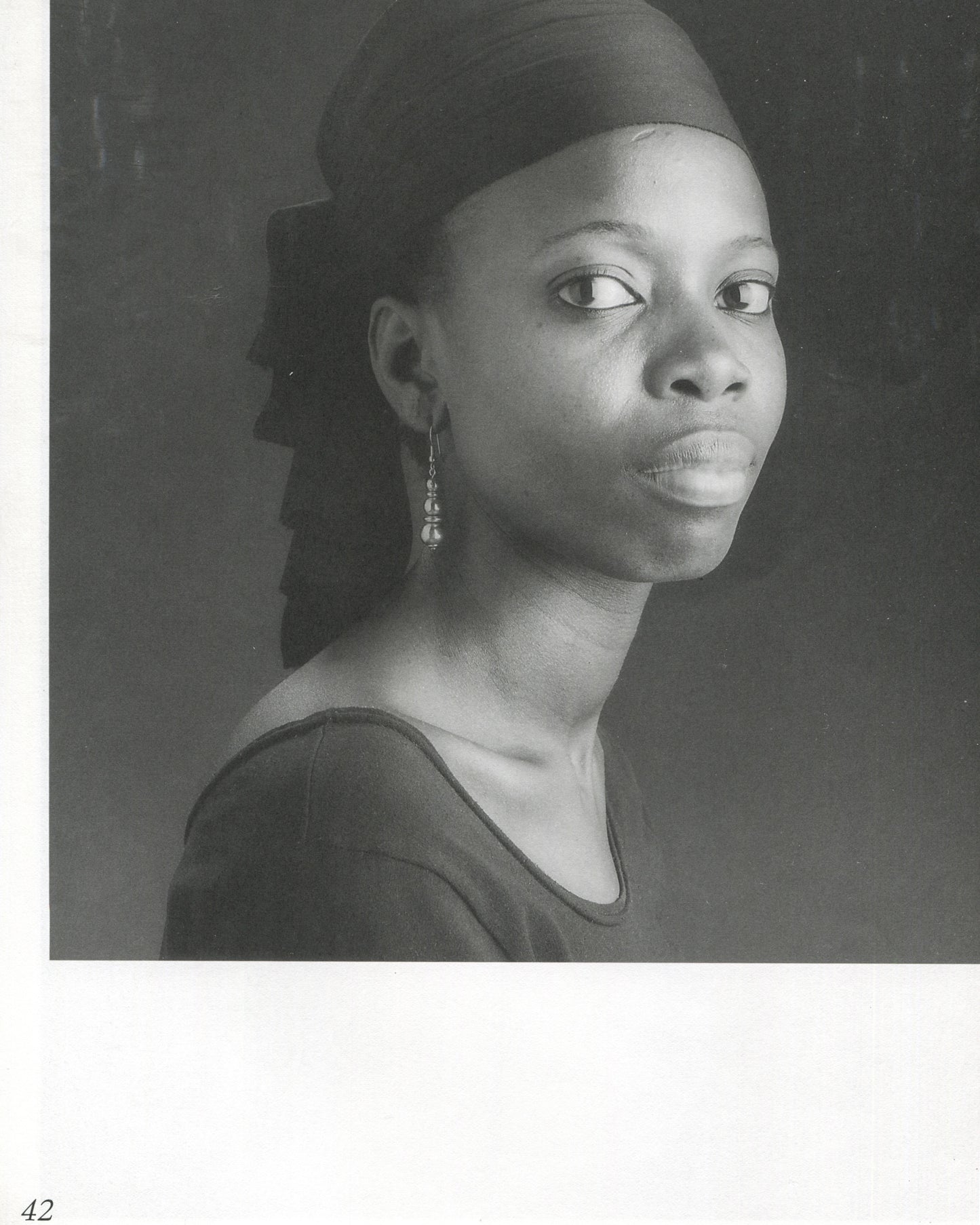  Interior page 42 from Robert Mapplethorpe, Some Women, Bulfinch Press, 1992, showing a black-and-white portrait of a Black woman in three-quarter profile, wearing a dark top and a close-fitting dark head covering with a long tail, a small drop earring visible, her gaze directed slightly upward and to the left, against a dark grey background, page number 42 at lower left.