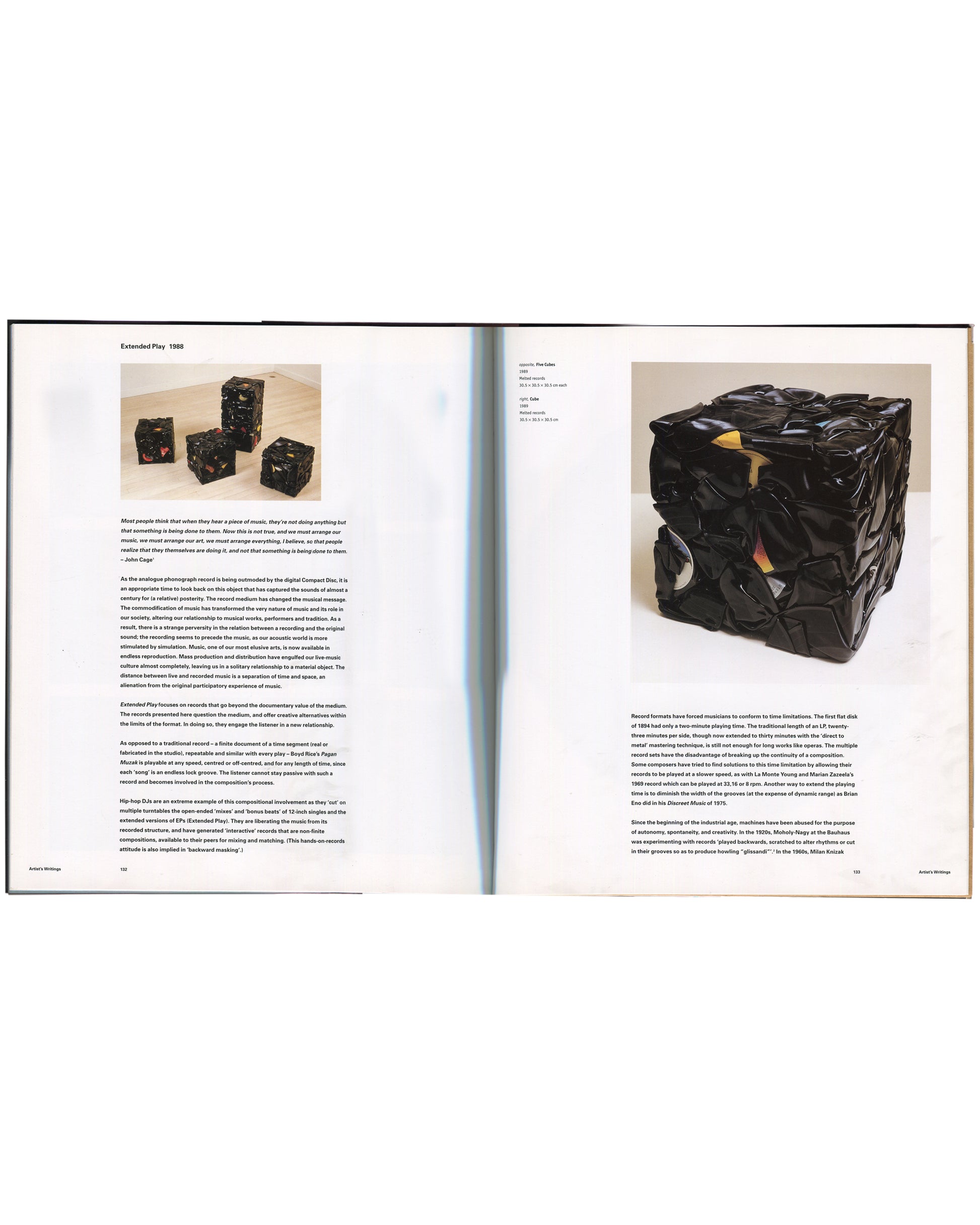  Interior spread from Christian Marclay, Phaidon Contemporary Artists Series, Phaidon Press, 2005, pages 132–133, showing the Artist's Writings section with the text of Extended Play, 1988, on the left page alongside a colour photograph of three small cube sculptures assembled from compressed and folded vinyl records, and on the right page a colour photograph of a large dark cube sculpture made from compressed vinyl records with visible record labels and edges protruding from its surface.