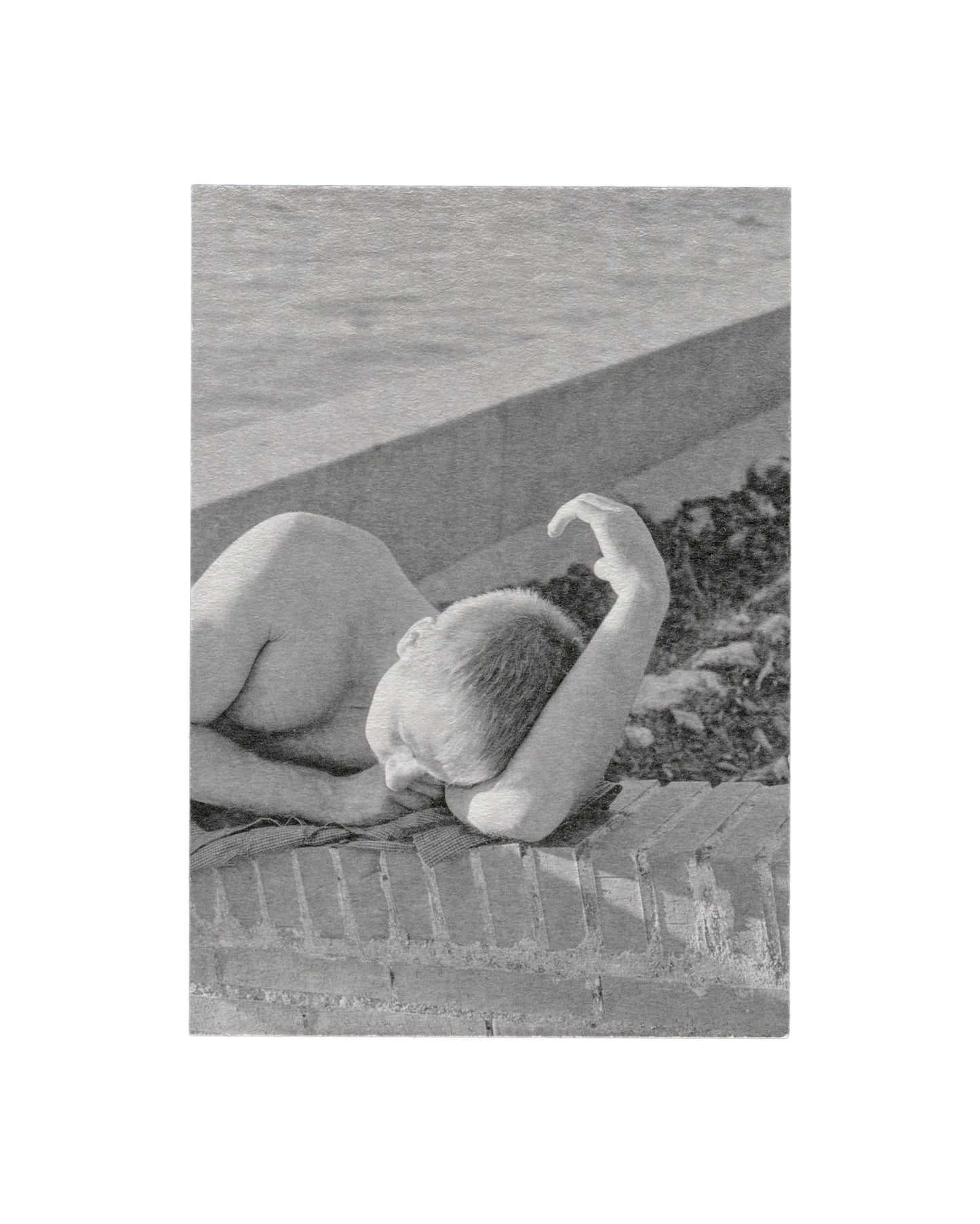 Recto Massao Mascaro, Untitled (Jardin #25), 2016. Galerie C Contemporary Art. Card recto: monochrome photograph on heavily textured card — a nude figure lying face-down on a brick ledge, head turned to one side, one arm raised; concrete surface and dark foliage visible behind; soft diffuse light; high-grain, low-contrast silver gelatin aesthetic.