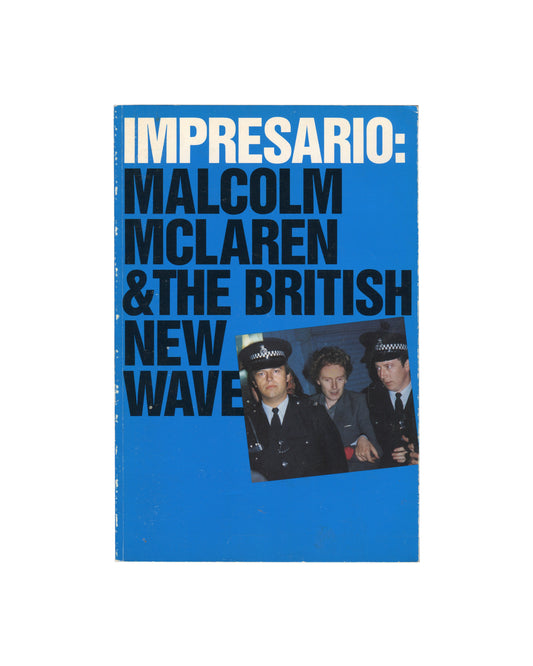 Exhibition catalogue cover, Impresario: Malcolm McLaren & The British New Wave, New Museum of Contemporary Art / The MIT Press, New York / Cambridge MA, 1988. Softcover with French flaps, 27 × 18 cm. Bright blue ground. Bold white and black sans-serif typography — 'IMPRESARIO:' upper left in white; 'MALCOLM / MCLAREN / & THE BRITISH / NEW / WAVE' in large black below. Inset colour photograph lower right — three figures in police uniforms, two in helmets, one in peaked cap; direct camera gaze. Rubbing and sc