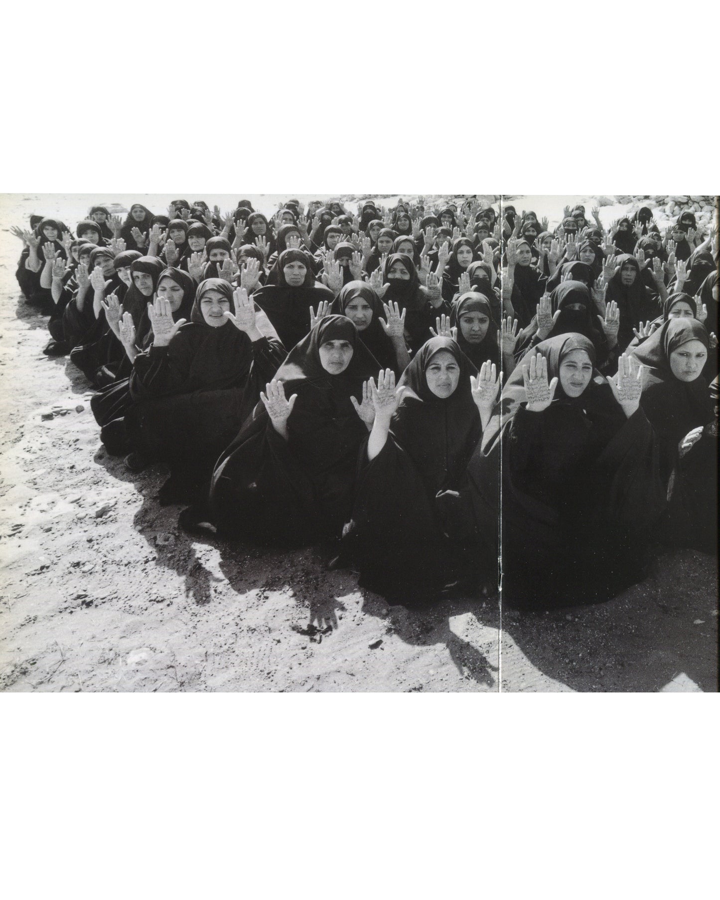 Shirin Neshat, Rapture, 1999, crowd of women in black chadors seated on ground, hands raised toward camera 