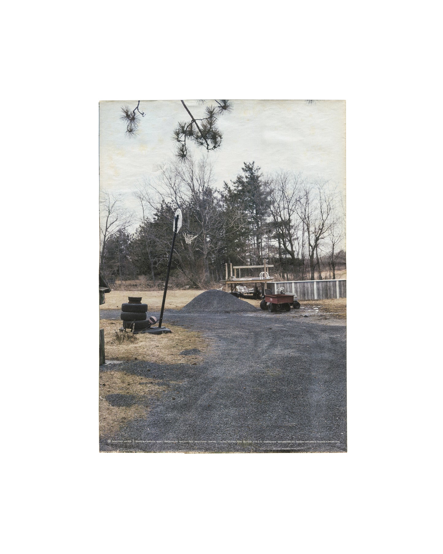 Back panel, Richard Prince, 3rd Place, Point d'Ironie no. 39, Agnès b. / Point d'Ironie, Paris, April 2006. Colour photograph — rural American yard, gravel drive, basketball hoop on tall pole, stacked tyres, pine trees, overcast sky; small text caption at lower edge. Light handling and fold lines as issued.