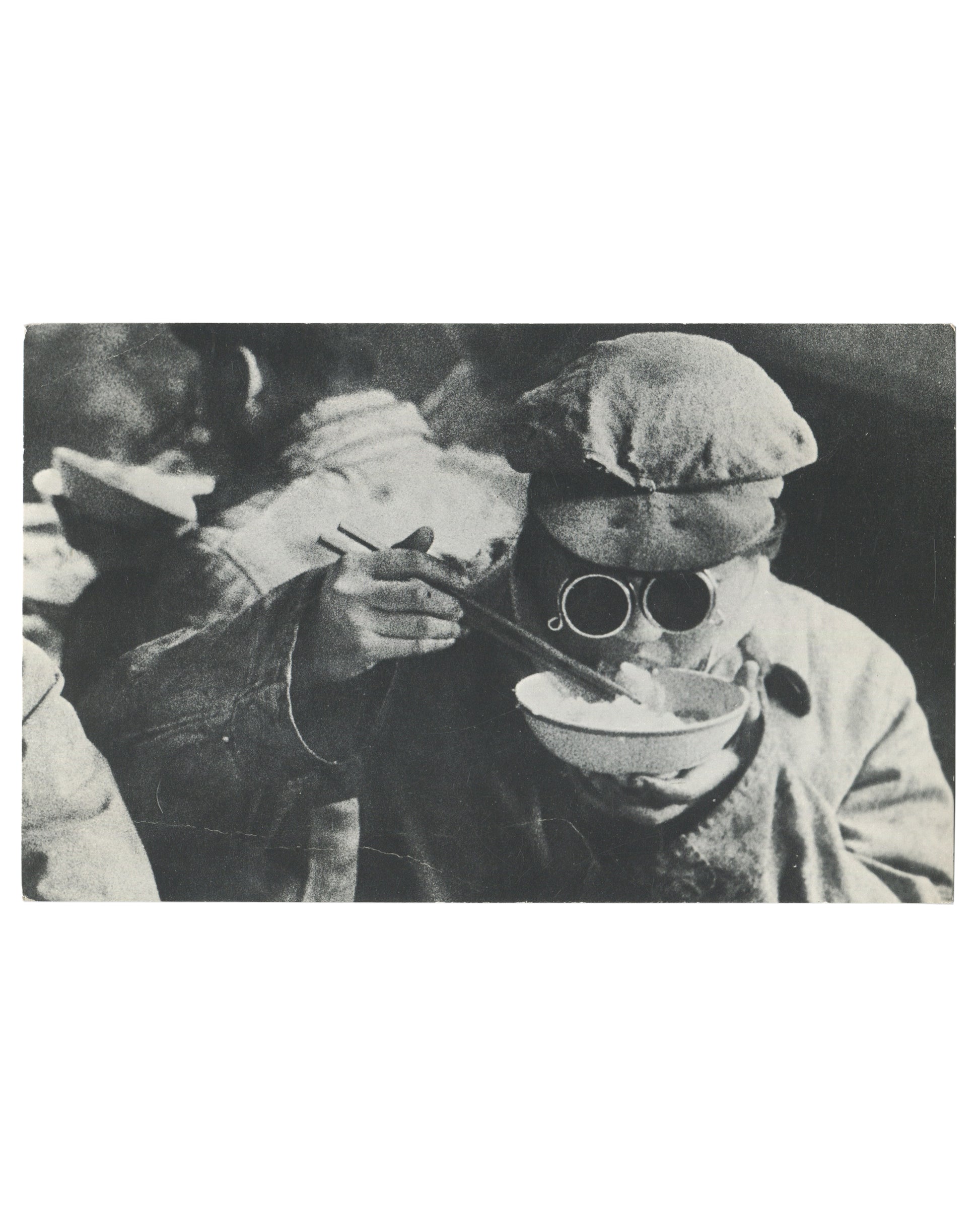 Original 1967 Galerie Delpire exhibition announcement card for Marc Riboud, Les trois bannières de la Chine, Paris, recto, full-bleed black-and-white photograph: two figures in heavy winter clothing and flat caps, one wearing round dark-lensed glasses and eating from a bowl with chopsticks, the other reaching toward them, both in close-up against a dark background.