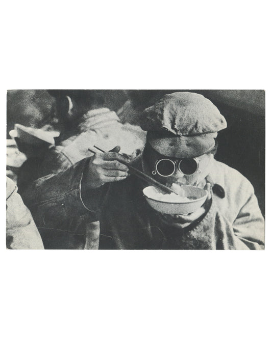 Original 1967 Galerie Delpire exhibition announcement card for Marc Riboud, Les trois bannières de la Chine, Paris, recto, full-bleed black-and-white photograph: two figures in heavy winter clothing and flat caps, one wearing round dark-lensed glasses and eating from a bowl with chopsticks, the other reaching toward them, both in close-up against a dark background.