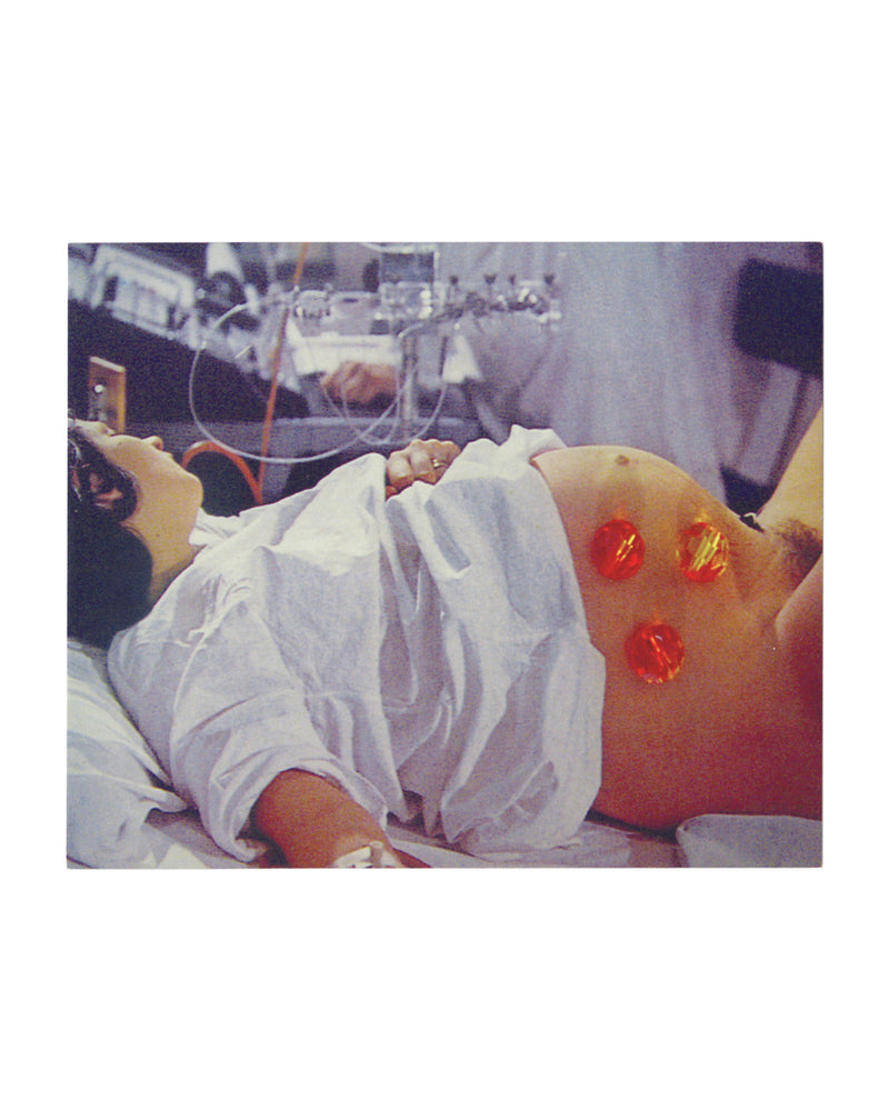 Pipilotti Rist, Heroes of Birth, exhibition announcement card recto. Luhring Augustine, New York, 2010. Colour photograph: a woman in a white hospital gown lies reclined, head tilted back, dark hair spread behind her. Her bare, heavily pregnant abdomen is visible, with three red circular monitoring devices attached to the skin. Medical equipment including tubing and IV lines visible in the background. Clinical setting, warm analogue colour palette. Image from Pipilotti Rist video work.
