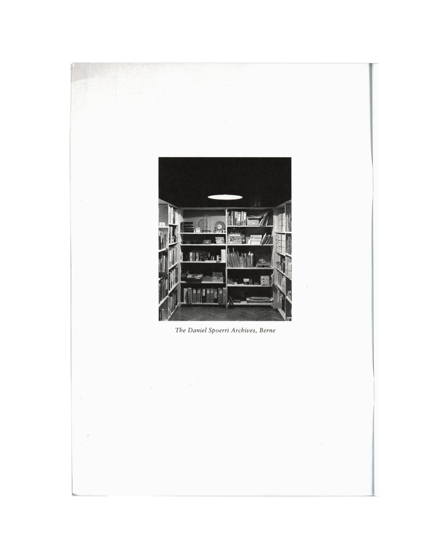 Daniel Spoerri, Profession Obsession 1997, interior: b&w photo of The Daniel Spoerri Archives Berne — shelves of books, binders and objects, oval ceiling light

