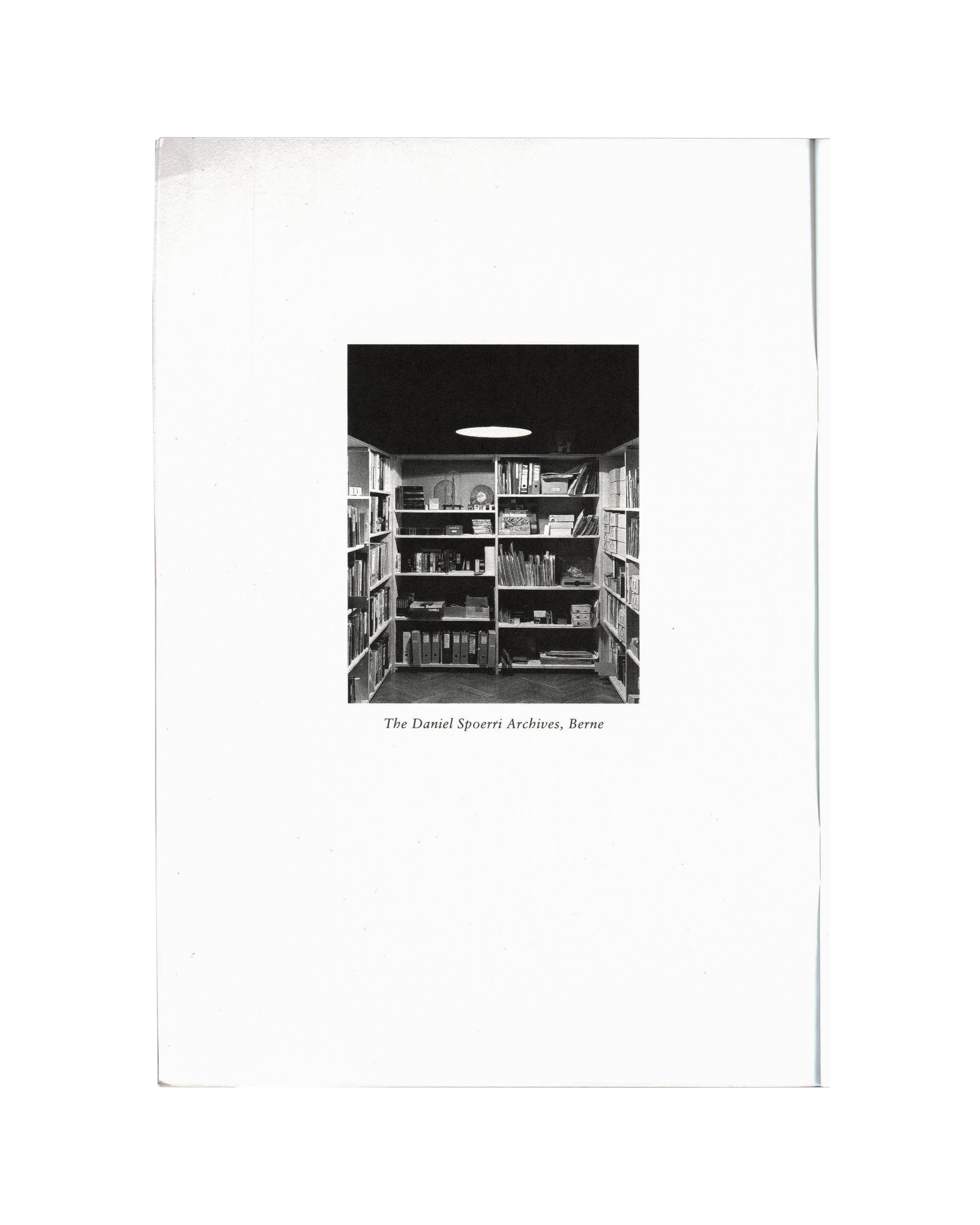 Daniel Spoerri, Profession Obsession 1997, interior: b&w photo of The Daniel Spoerri Archives Berne — shelves of books, binders and objects, oval ceiling light
