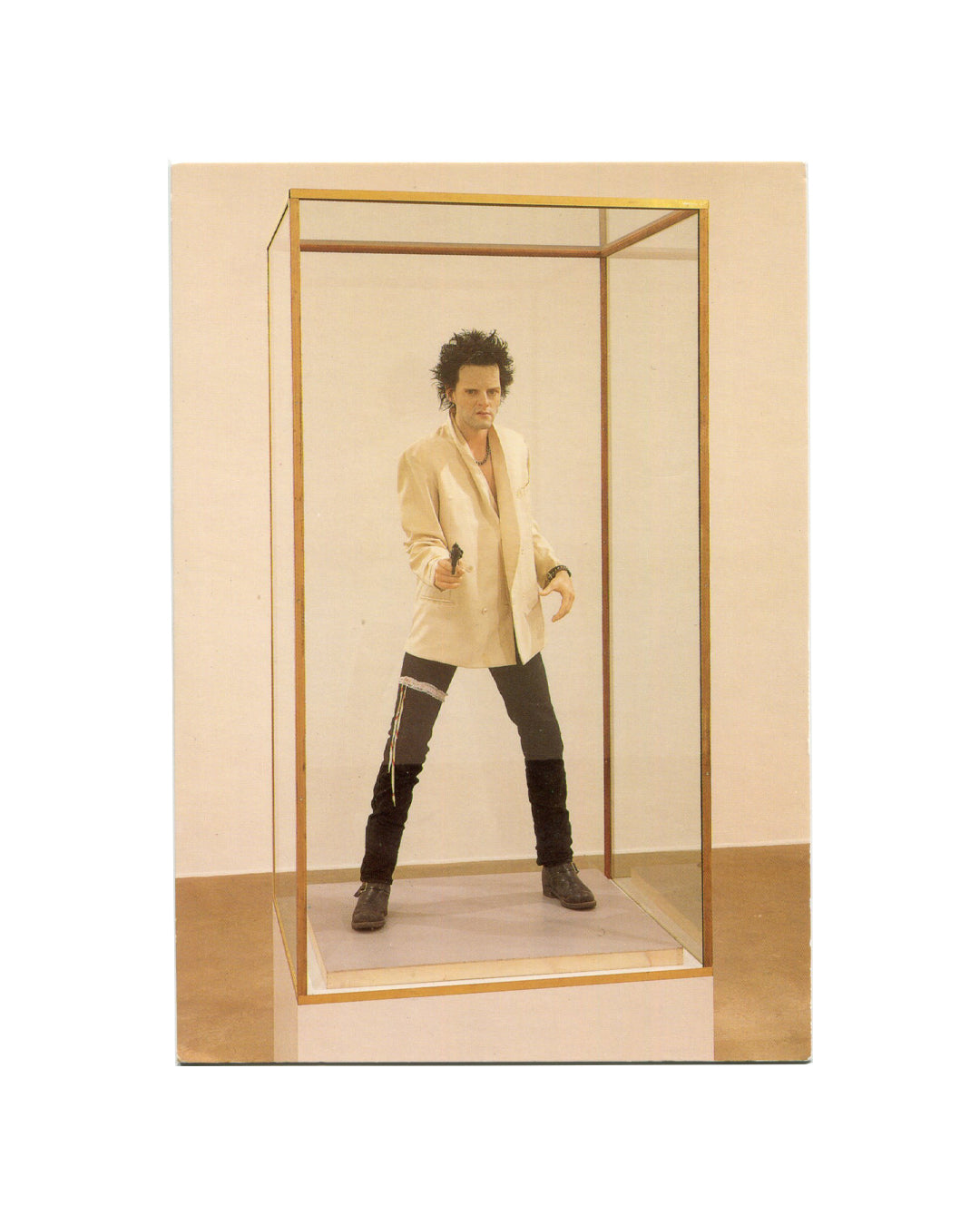 Saatchi Collection postcard reproducing Gavin Turk Pop (1993). Colour photograph of wax self-portrait figure encased in brass-framed glass vitrine: figure in white blazer, dark trousers and boots, wild dark hair, holding a gun toward the viewer in a wide stance; gallery floor and white wall visible behind; photograph by Hugo Glendinning.