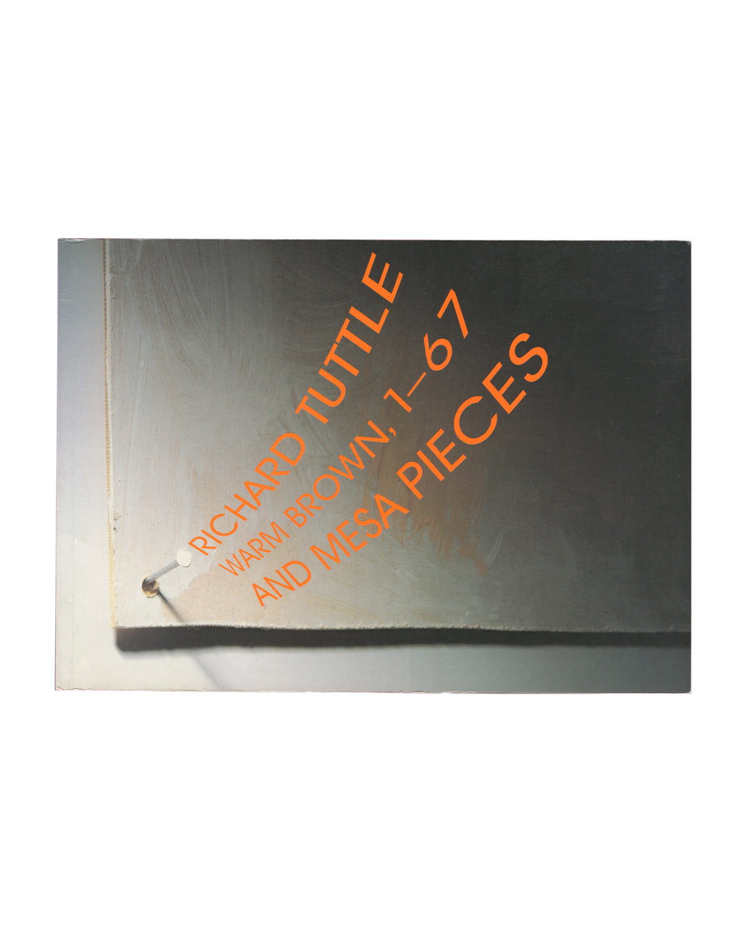 Cover of Richard Tuttle, Warm Brown, 1–67 and Mesa Pieces, Kärntner Landesgalerie, Klagenfurt, c. 1990s, showing a close-up photograph of a metallic reflective surface — the cover of the catalogue itself — with the title RICHARD TUTTLE / WARM BROWN, 1–67 / AND MESA PIECES printed diagonally in large orange sans-serif capitals, and a single metal screw pin visible at lower left.