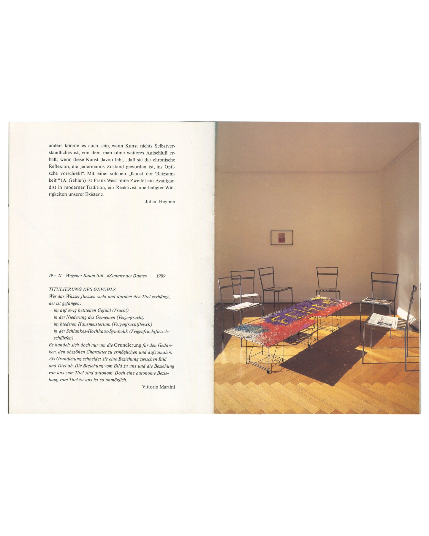 Interior spread, Franz West, Museum Haus Lange, Heft 1, 1989. Left page: German essay text in small serif type — Julian Heynen text on West's practice, ending with attribution 'Julian Heynen'; below, caption 'Wegener Raum 6/6 »Zimmer der Dame« 1989' and poem 'TITULIERUNG DES GEFÜHLS' by Vittorio Martini in italic type. Right page: colour installation photograph — white gallery room with herringbone parquet floor; six wire-frame chairs arranged around a large low table covered with a colourful textile work i