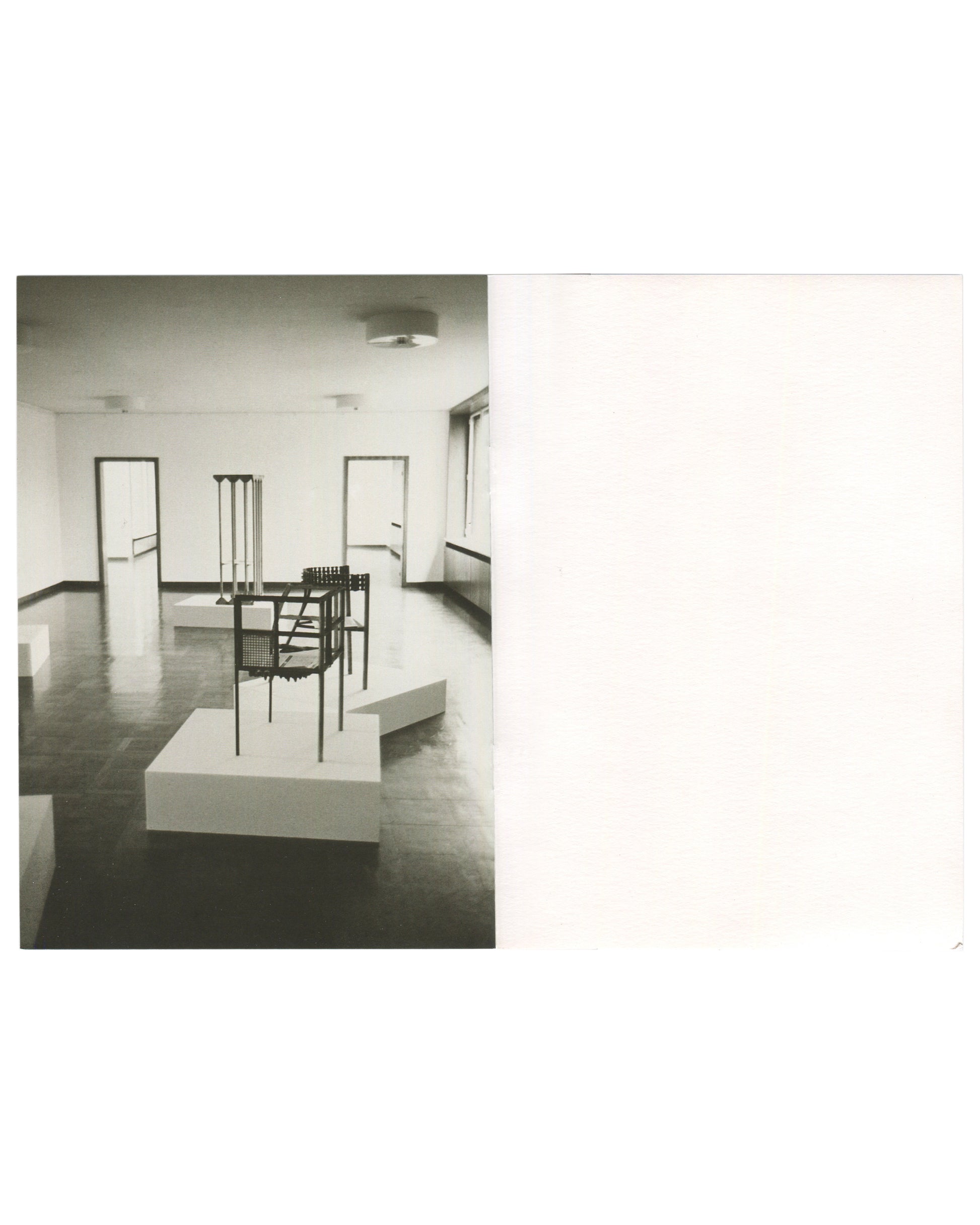 Interior spread, Franz West, Museum Haus Lange, Heft 2, Krefelder Kunstmuseen, Krefeld, 1989. Black-and-white installation photograph by Günther Förg — wire-frame and perforated-metal chair sculpture on white plinth foreground; tall multi-legged stool form on plinth behind; dark reflective floor, white walls, two doorways visible. Right page: blank white.