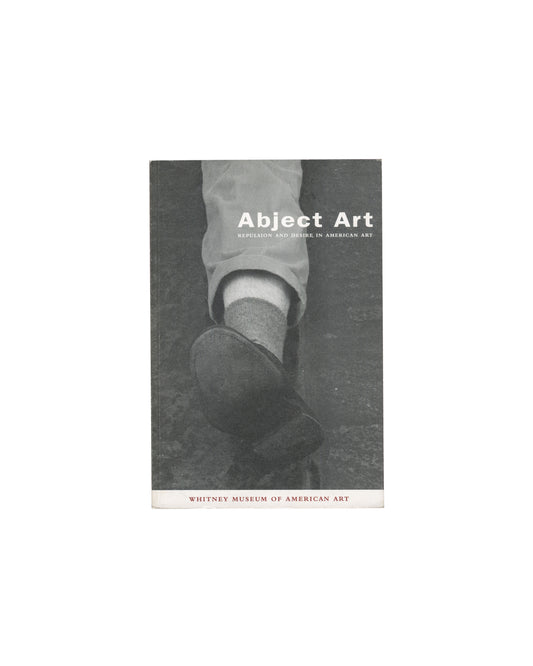  Robert Gober's severed leg sculpture — wax, cloth, shoe — against Warhol Oxidation Painting surface. Title "Abject Art / Repulsion and Desire in American Art" and "Whitney Museum of American Art" in type.