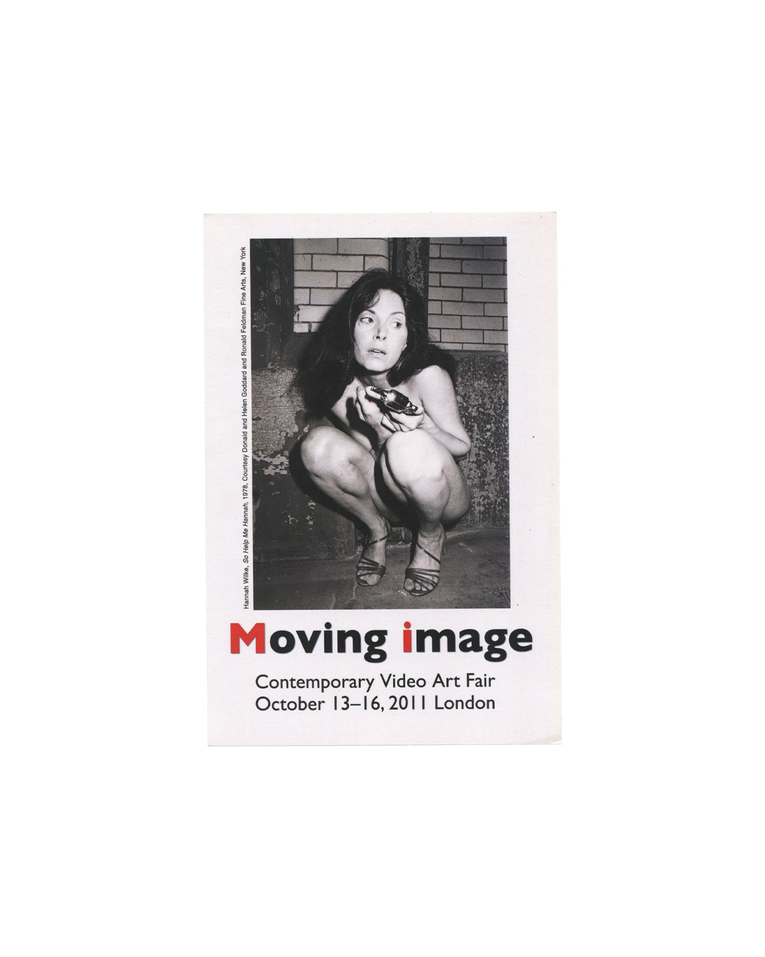 Front Moving Image Contemporary Video Art Fair, London, 2011, announcement card, front, white card: black-and-white photograph of Hannah Wilke crouching against a brick wall, holding a shoe, from So Help Me Hannah, 1978; Moving image in large type below with M and i in red; Contemporary Video Art Fair / October 13–16, 2011 London in black sans-serif; vertical caption at left edge: Hannah Wilke, So Help Me Hannah, 1978. Courtesy Donald and Helen Goddard and Ronald Feldman Fine Arts, New York.