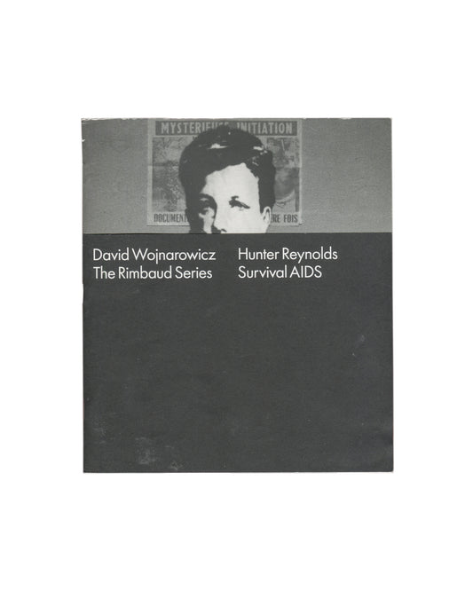 David Wojnarowicz / Hunter Reynolds, The Rimbaud Series / Survival AIDS, P.P.O.W Gallery, New York, 2012. Artist publication / exhibition catalogue, softcover, approx. 20 × 23 cm, 16 pages. Design by Project Projects. Two-panel cover: upper half, grey band with cropped black-and-white photograph — masked figure (Arthur Rimbaud mask) against a wall bearing a partially visible poster reading 'MYSTERIOUS INITIATION' and 'DOCUMENT… RE FOIS'; lower half, dark charcoal ground with white sans-serif text in two col