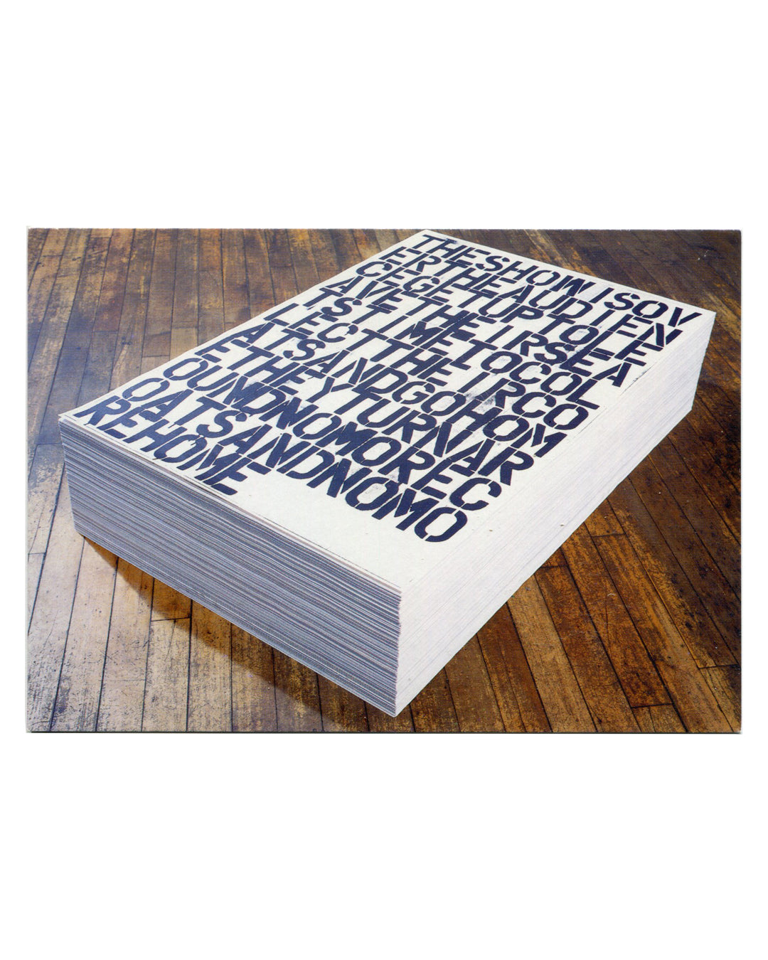 Exhibition postcard from TRAUMA, Dundee Contemporary Arts, 2001. Recto: installation photograph of Christopher Wool / Felix Gonzalez-Torres Untitled (1991) — a large stack of white offset-printed sheets on a wooden floor, top sheet bearing dense black compressed text reading 'THE SHOW IS OVER THE AUDIENCE GET UP TO LEAVE THEIR SEATS TIME TO COLLECT THEIR COATS AND GO HOME AND GO HOME AND GO HOME AND NO MORE.