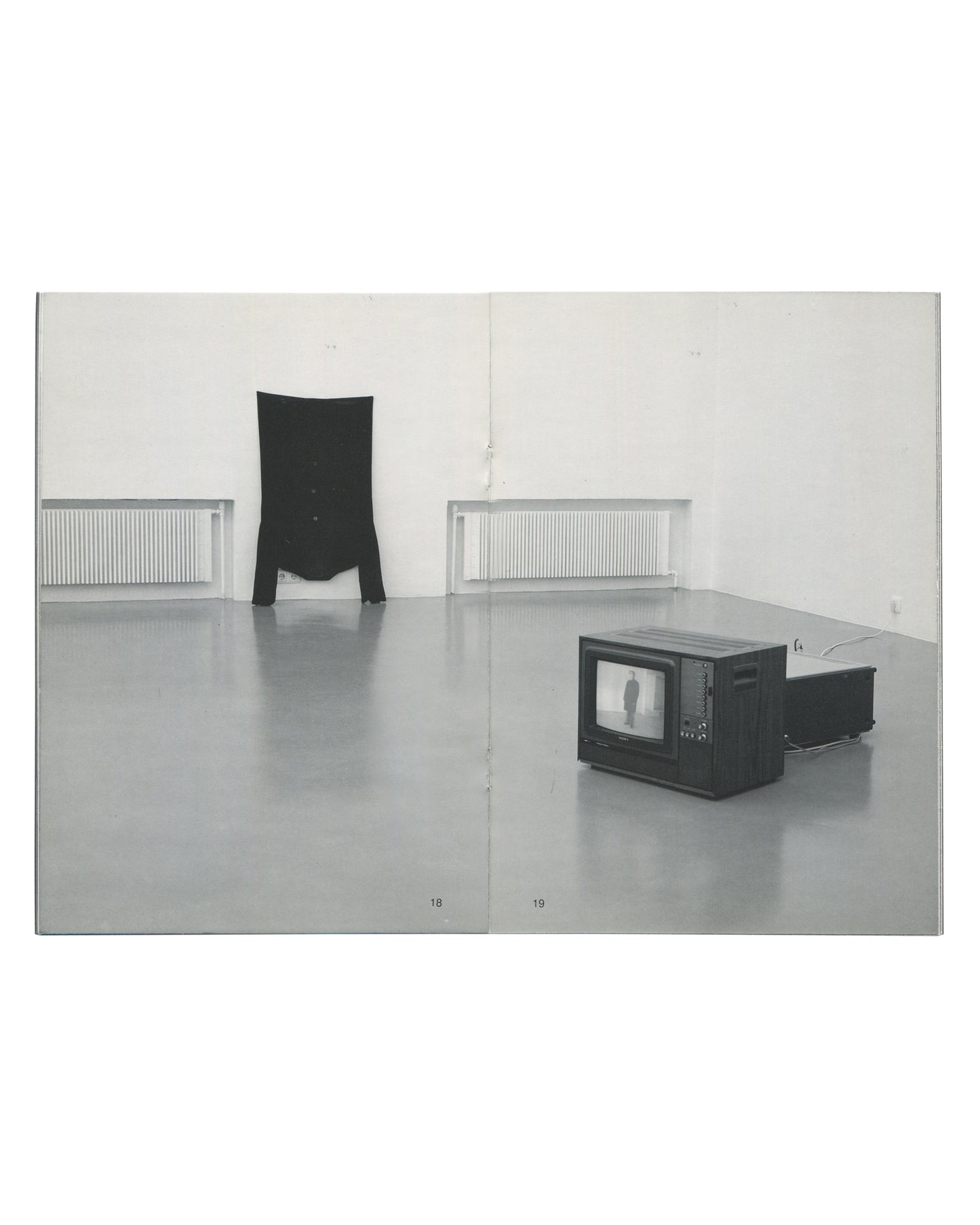 Interior spread of Erwin Wurm, Kunstverein in Hamburg / Villa Arson, 1993, pages 18–19, showing a colour installation photograph of a white gallery space with two works: a black garment standing upright without a body on the left wall, and a small CRT television monitor on a low trolley showing a figure on screen to the right.