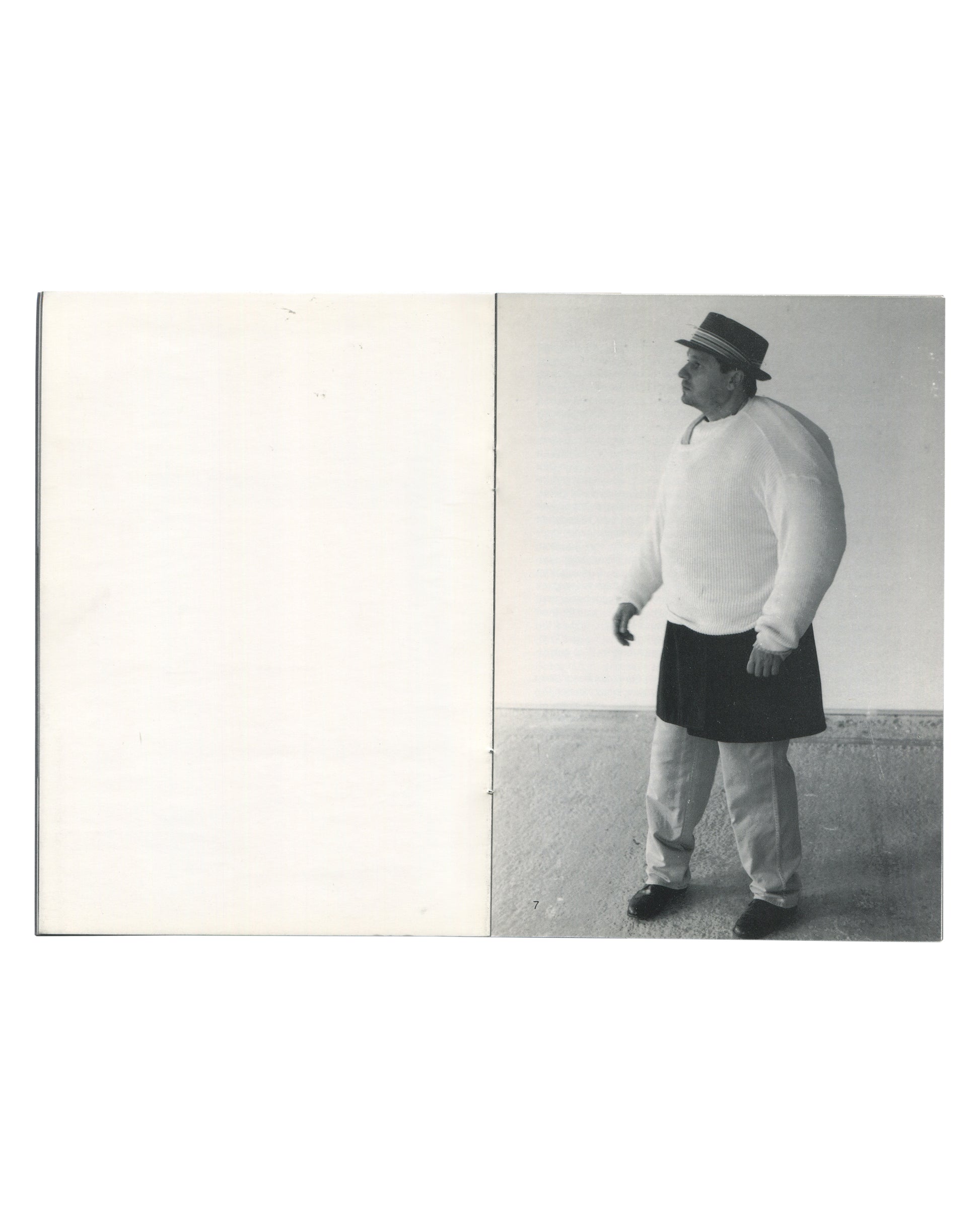 Interior spread of Erwin Wurm, Kunstverein in Hamburg / Villa Arson, 1993, page 7, left page blank white, right page showing a black-and-white photograph of a man wearing a hat, white knitted sweater, and dark skirt over trousers, standing outdoors on a sandy surface and looking to the left.