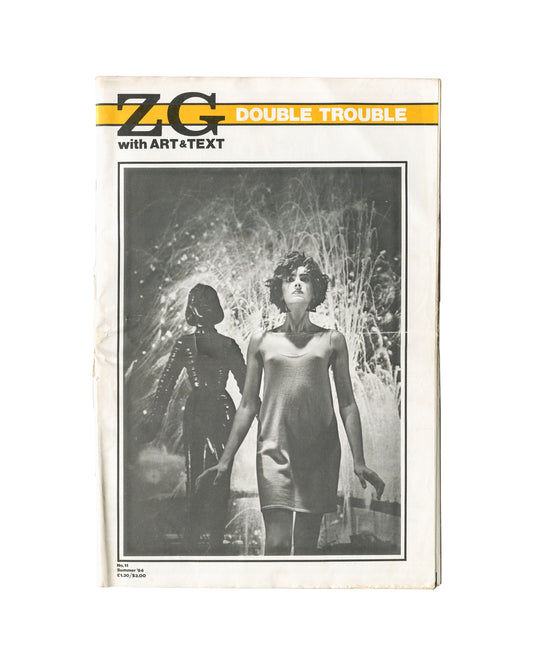 Magazine cover, ZG No. 11 / Art & Text 15: Double Trouble, ZG Magazine / Art & Text, New York / Melbourne, 1984. Edited by Rosetta Brooks. Large-format staple-bound periodical, 28 × 42 cm. Yellow horizontal band upper third — bold black 'ZG' logotype left; white sans-serif 'DOUBLE TROUBLE' right; below band: 'with ART&TEXT'. Full-bleed black-and-white photograph — two female figures in hazy backlit environment; foreground figure in short slip dress, short dark hair; background figure in dark structured outf